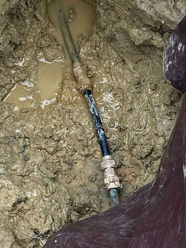 Pipes joined with fittings in muddy ground. Water and mud surround the pipes.