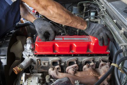 Mechanic installing a red car valve cover in an engine bay