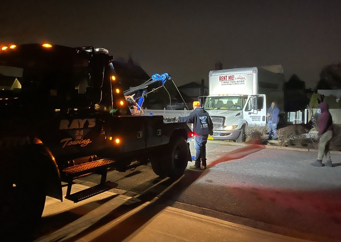 A tow truck is parked on the side of the road at night.