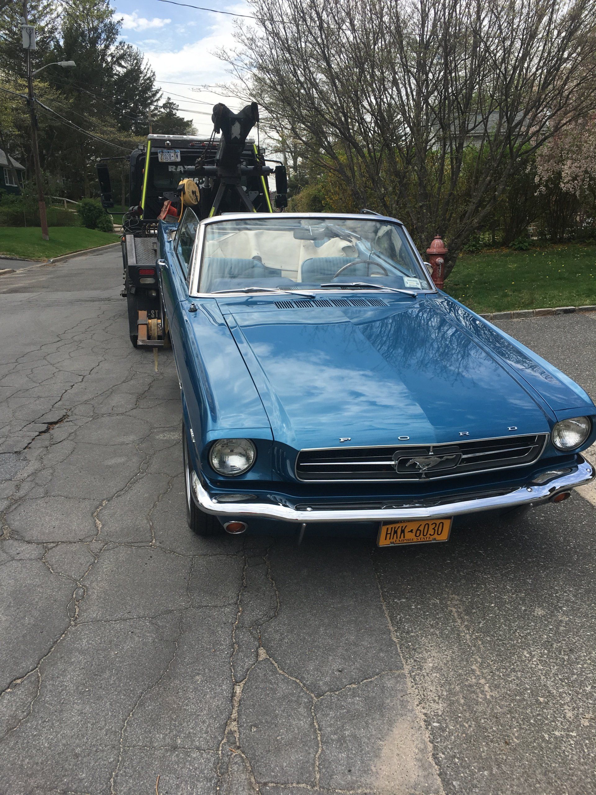 A blue car is being towed down a street by a tow truck.