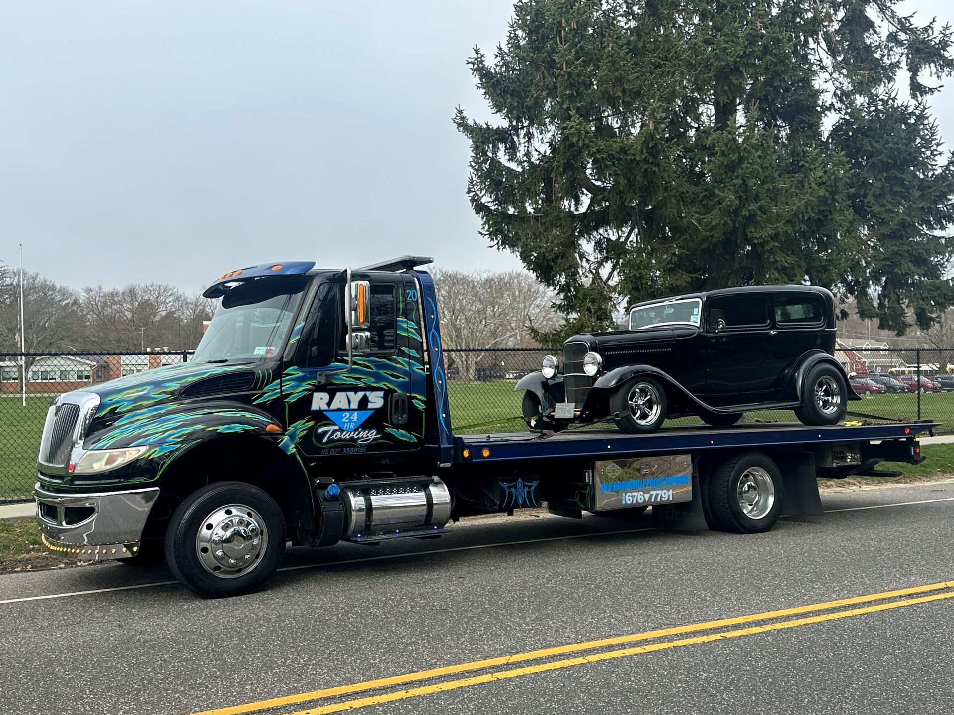 A tow truck is carrying a black car on the back of it.