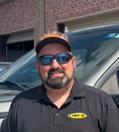 Man wearing sunglasses and hat, smiling, standing in front of vehicle.