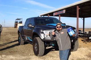 Man with a thumbs-up stands by a dark truck.