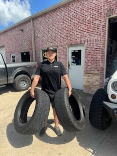Man holding two tires in front of a brick building.