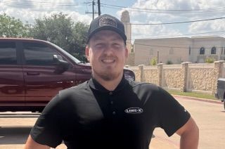 Man in black shirt and cap smiling outdoors, near a red truck.