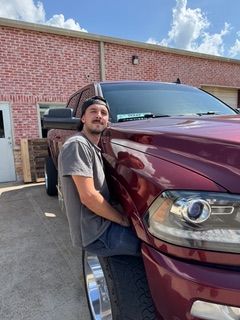 Man sitting on the front tire of a red pickup truck, smiling.