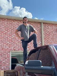 Man standing on a truck bed in front of a brick building.
