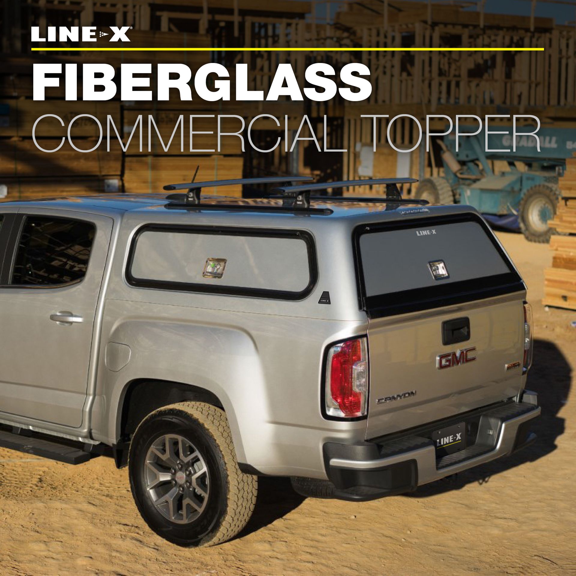 Silver GMC truck with a LINE-X fiberglass commercial topper, roof rack, and a construction site background.