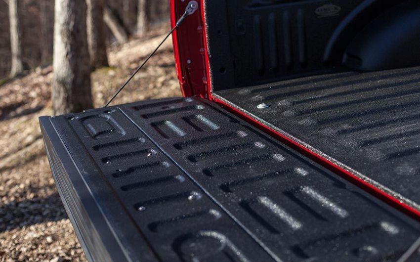 The back of a red truck with the bed open in the woods.