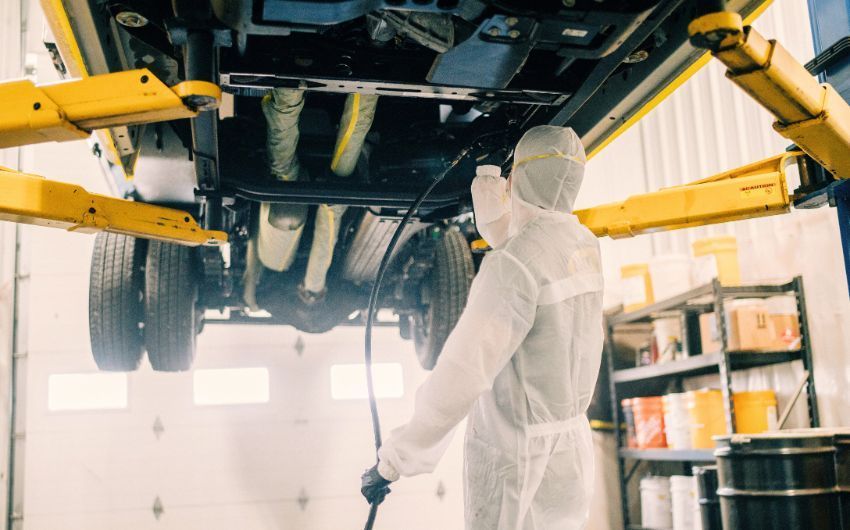 A man in a protective suit is spraying a car in a garage.