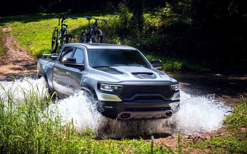A ram truck is driving through a puddle of water on a dirt road.