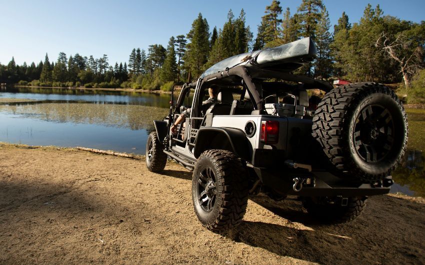 A jeep is parked on the beach next to a lake.