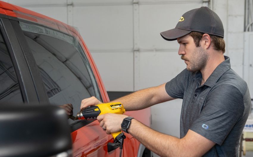 A man is applying window tinting to a red truck.