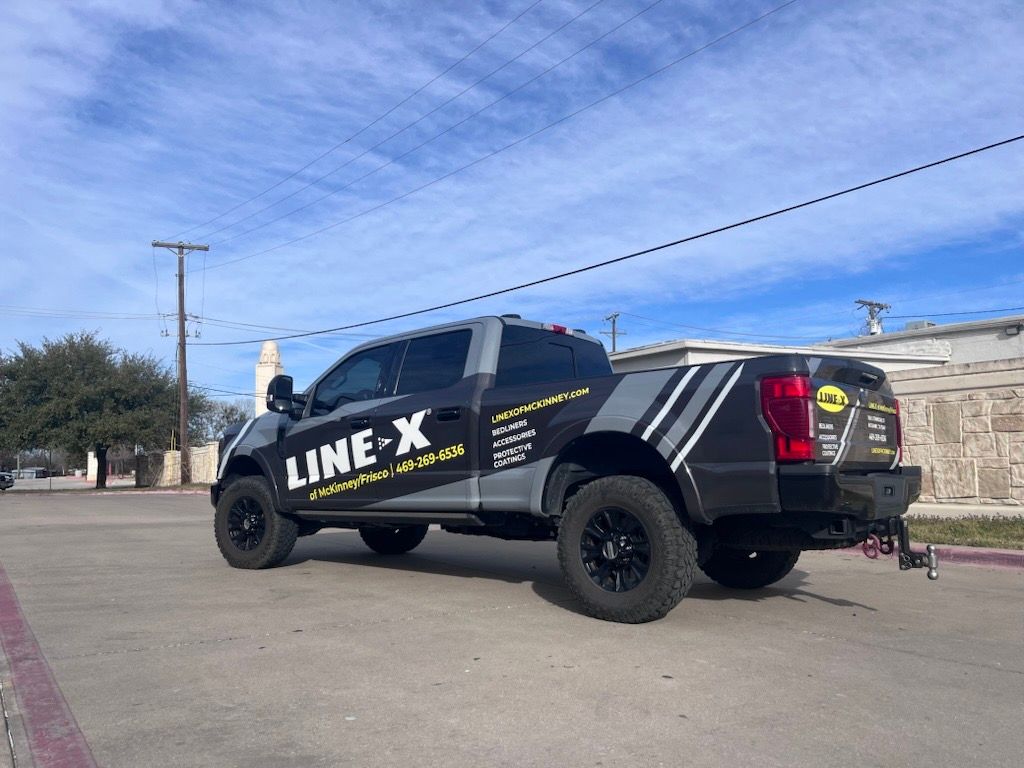 A black truck with the word line x on the side is parked in a parking lot.