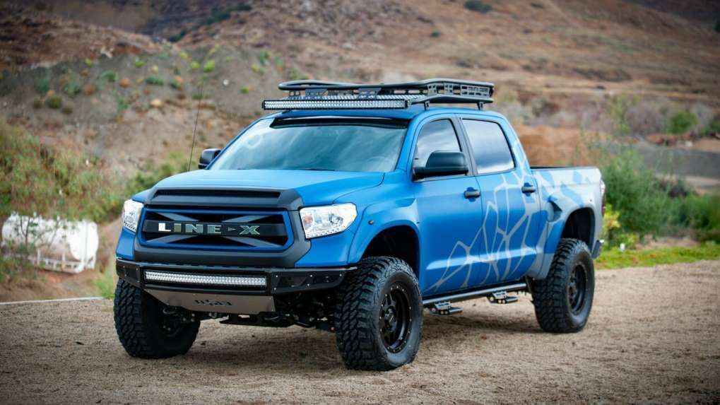A blue truck with a roof rack is parked on a dirt road.