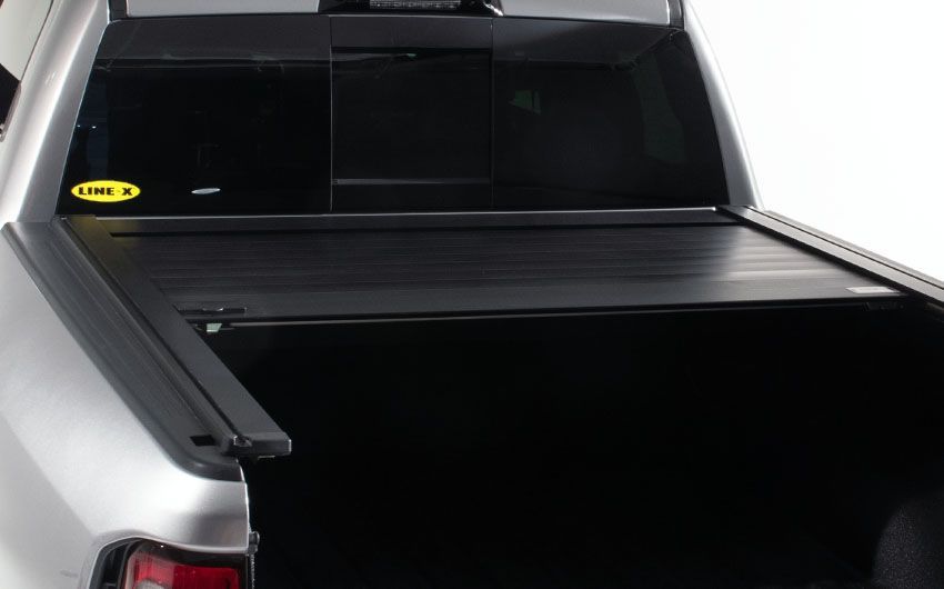 A silver truck with a black bed cover on it.