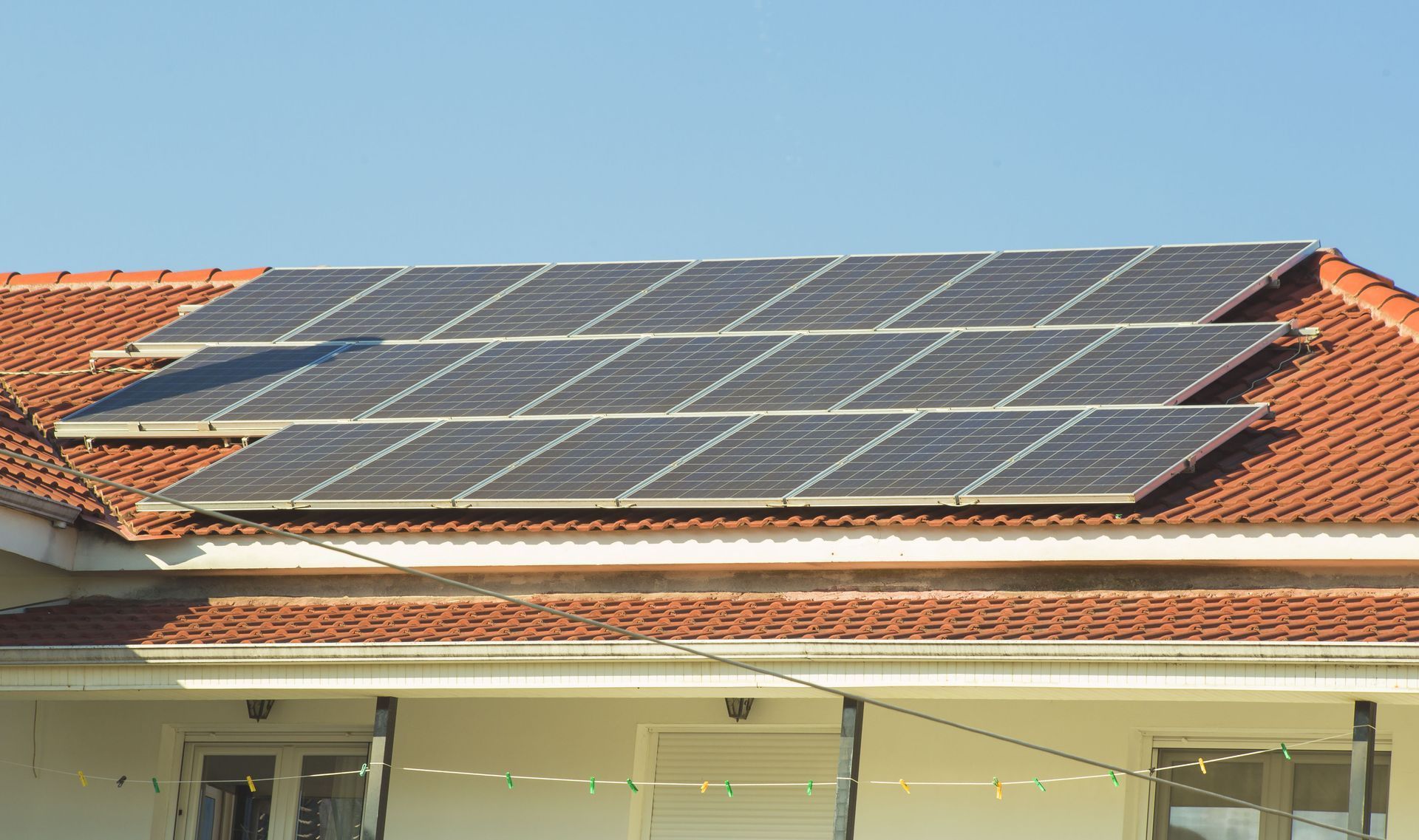 Solar panels installed on a red tiled house roof under a clear blue sky