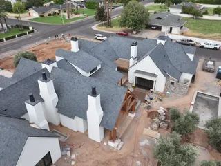 Aerial view of a large gray-roofed house with white walls and a damaged side wall in a suburban neighborhood