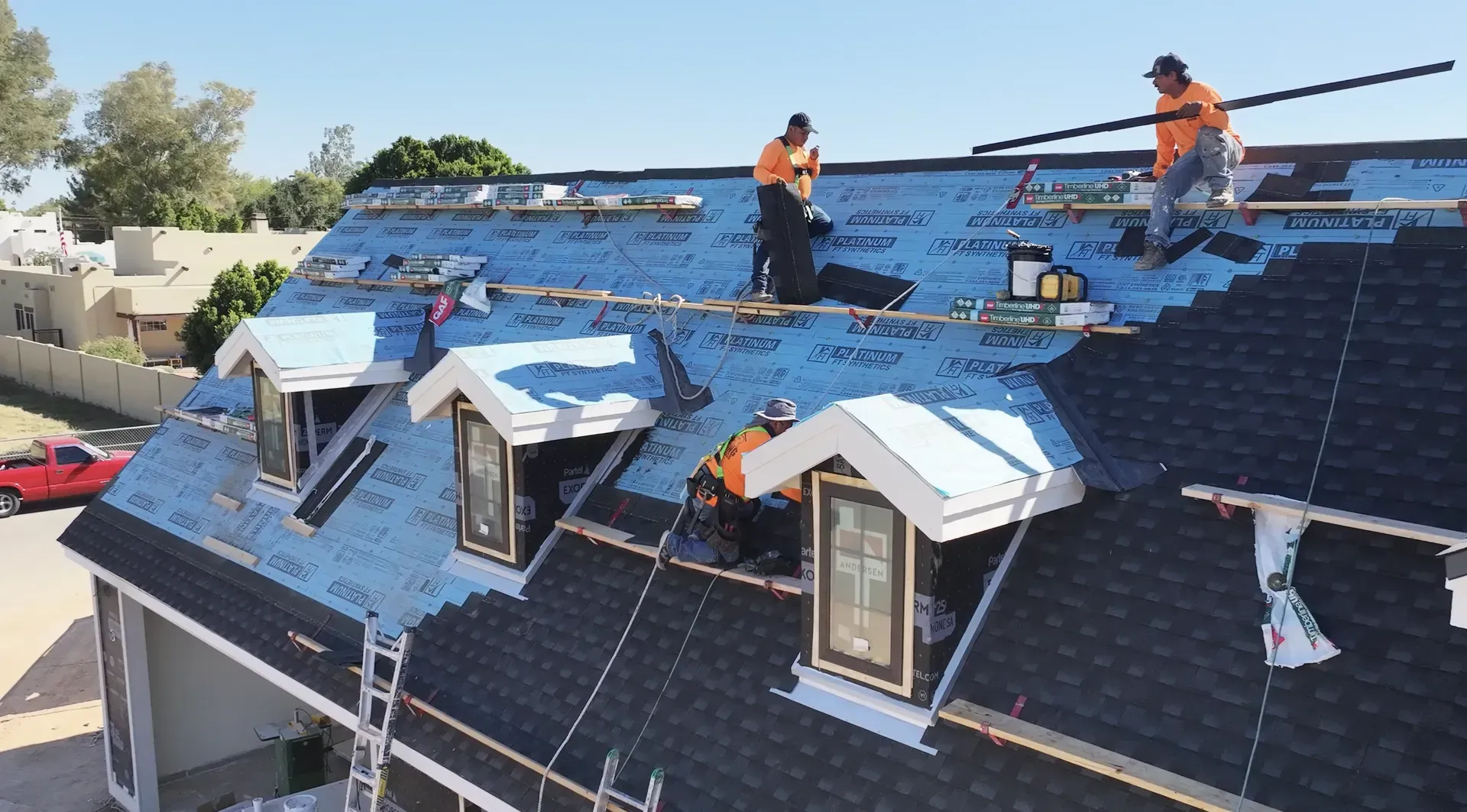 Workers installing blue solar panels on a rooftop with several dormer windows.