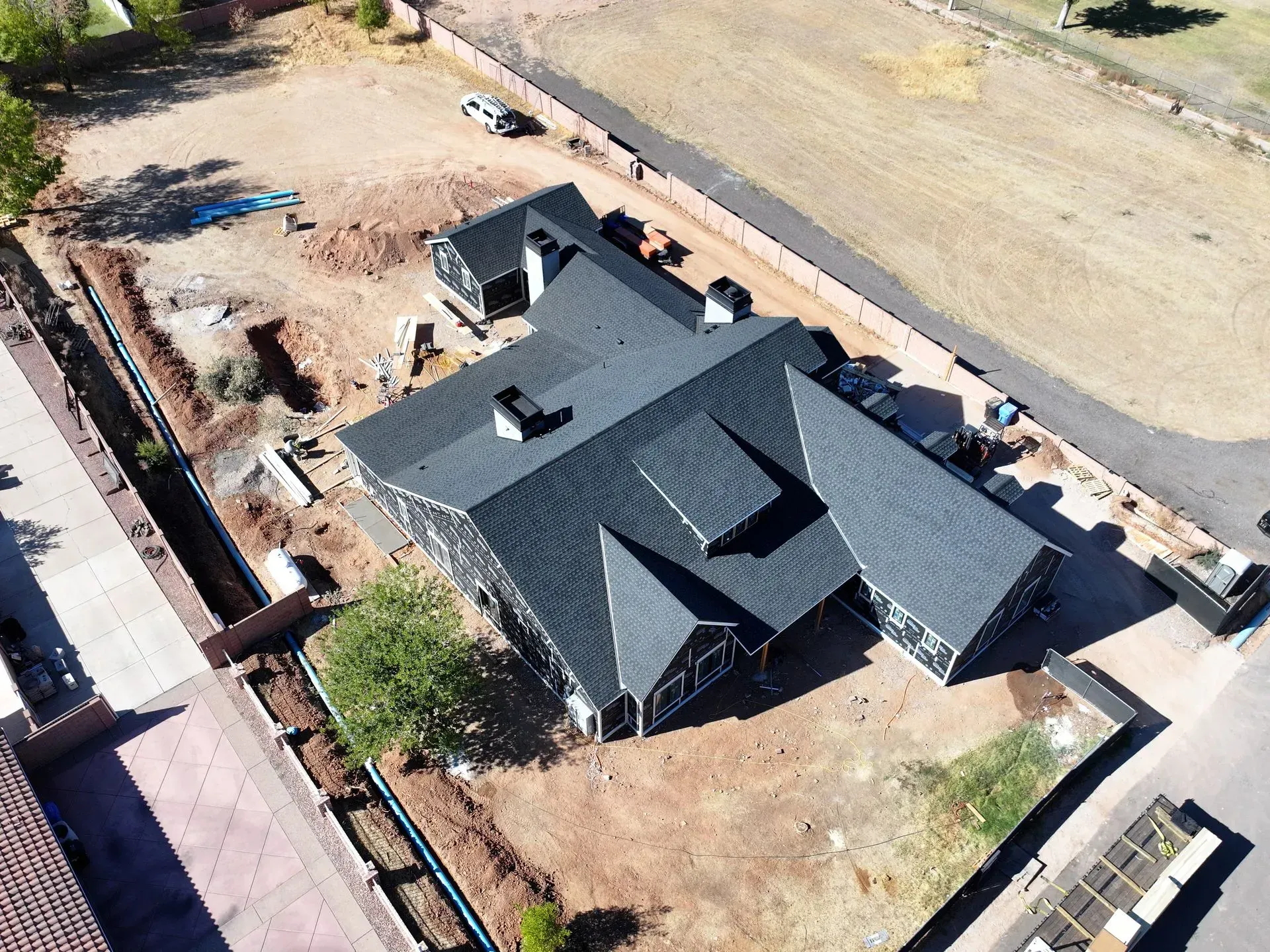 Aerial view of a dark-roofed house under construction in a fenced dirt lot.