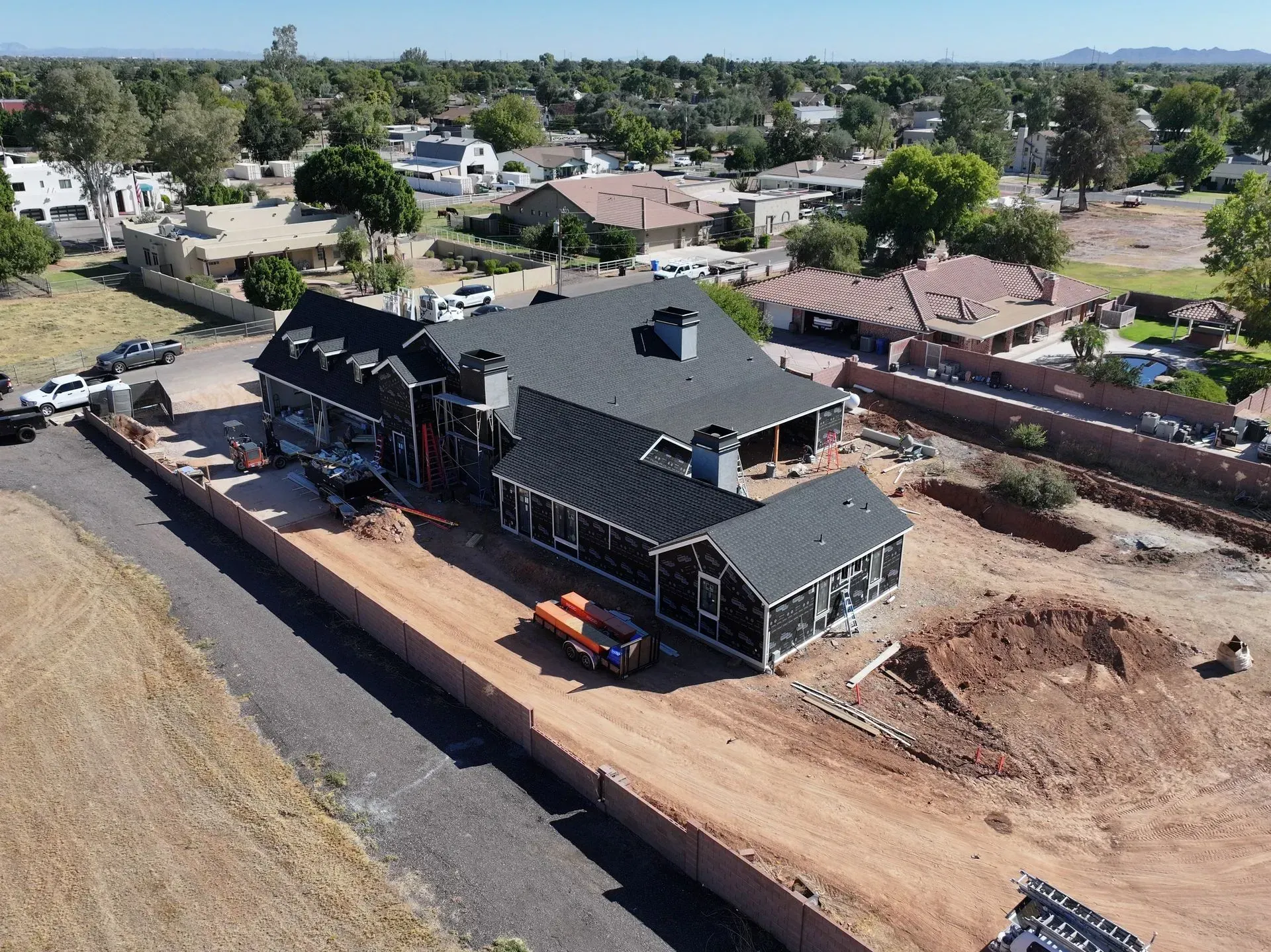 Aerial view of a house under construction with dark roof, dirt lot, and surrounding neighborhood.