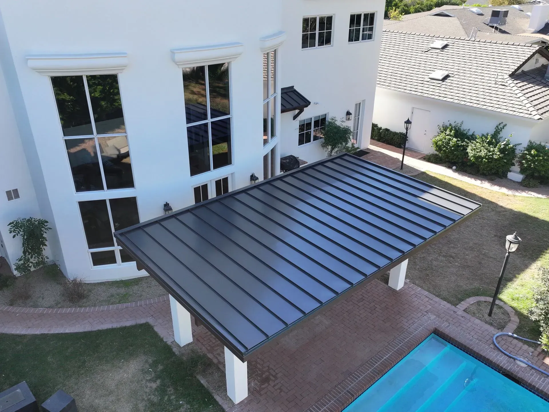 Modern white house with a dark metal patio roof beside a swimming pool and landscaped yard