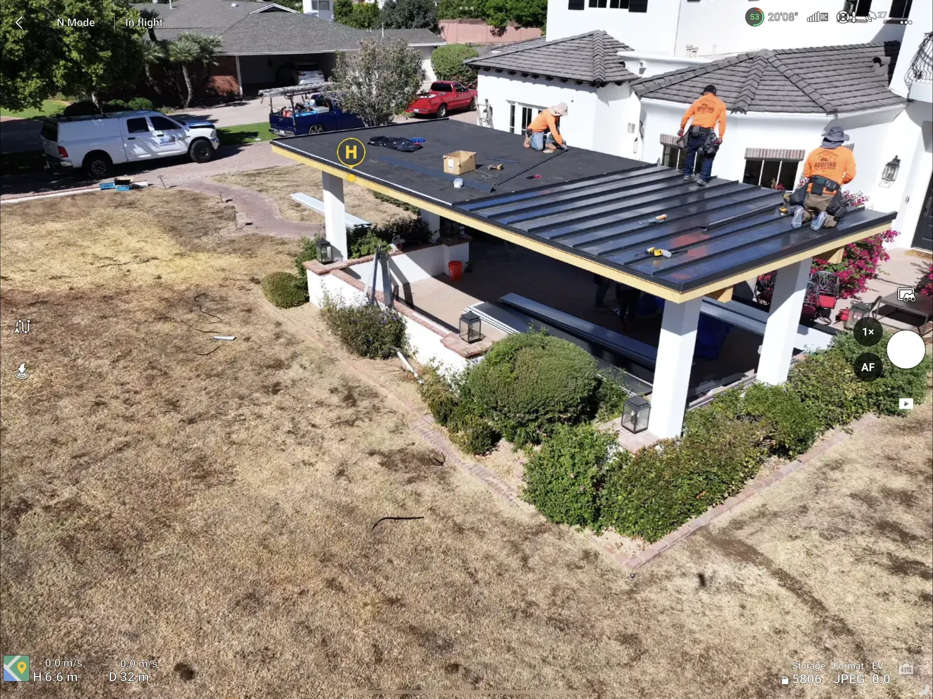 Roofing crew installing a black roof on a white house beside a dry, grassy lot.