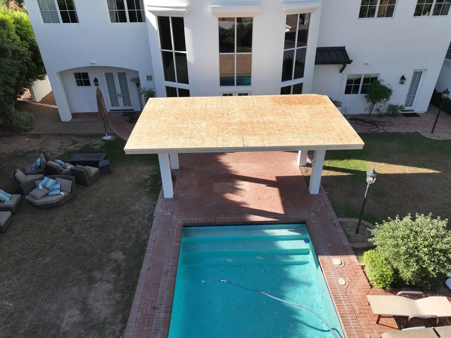 Poolside patio with a wooden canopy beside a turquoise pool and a white house courtyard