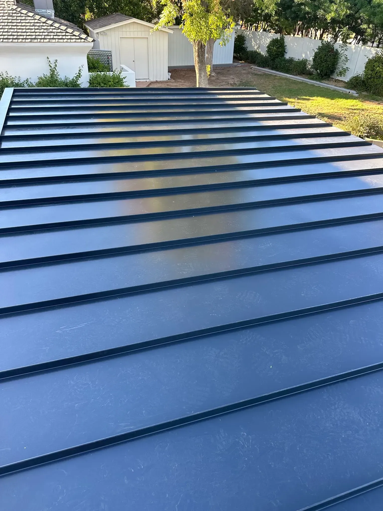 Blue metal roof panels with skylight strips in a backyard, with trees and a garage in the background