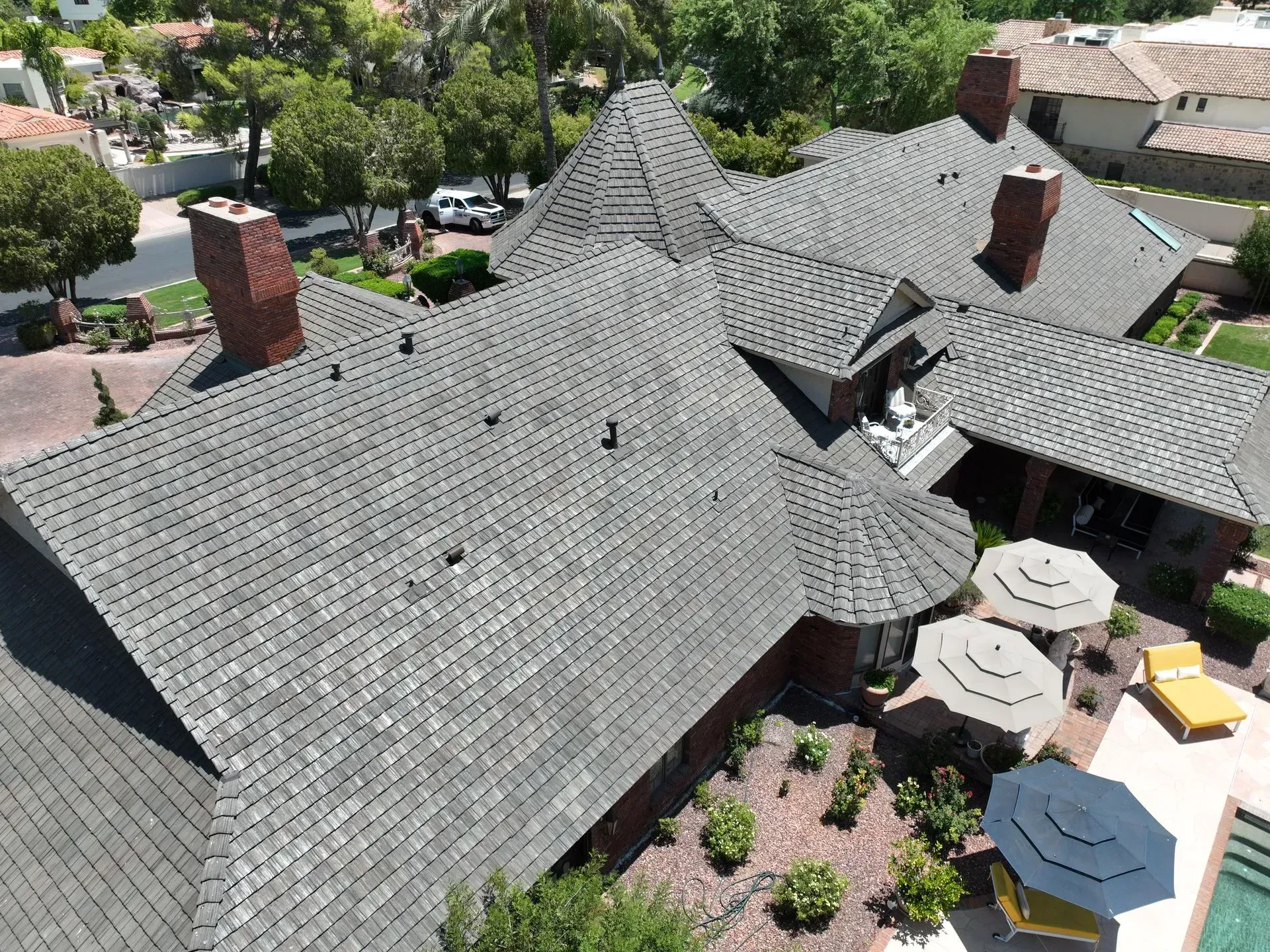 Aerial view of a large shingled house with brick chimneys and a patio with white umbrellas.