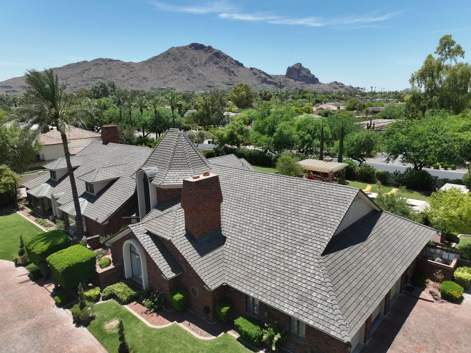 Desert-style house with gray shingle roof, brick chimney, and mountain view under a clear blue sky