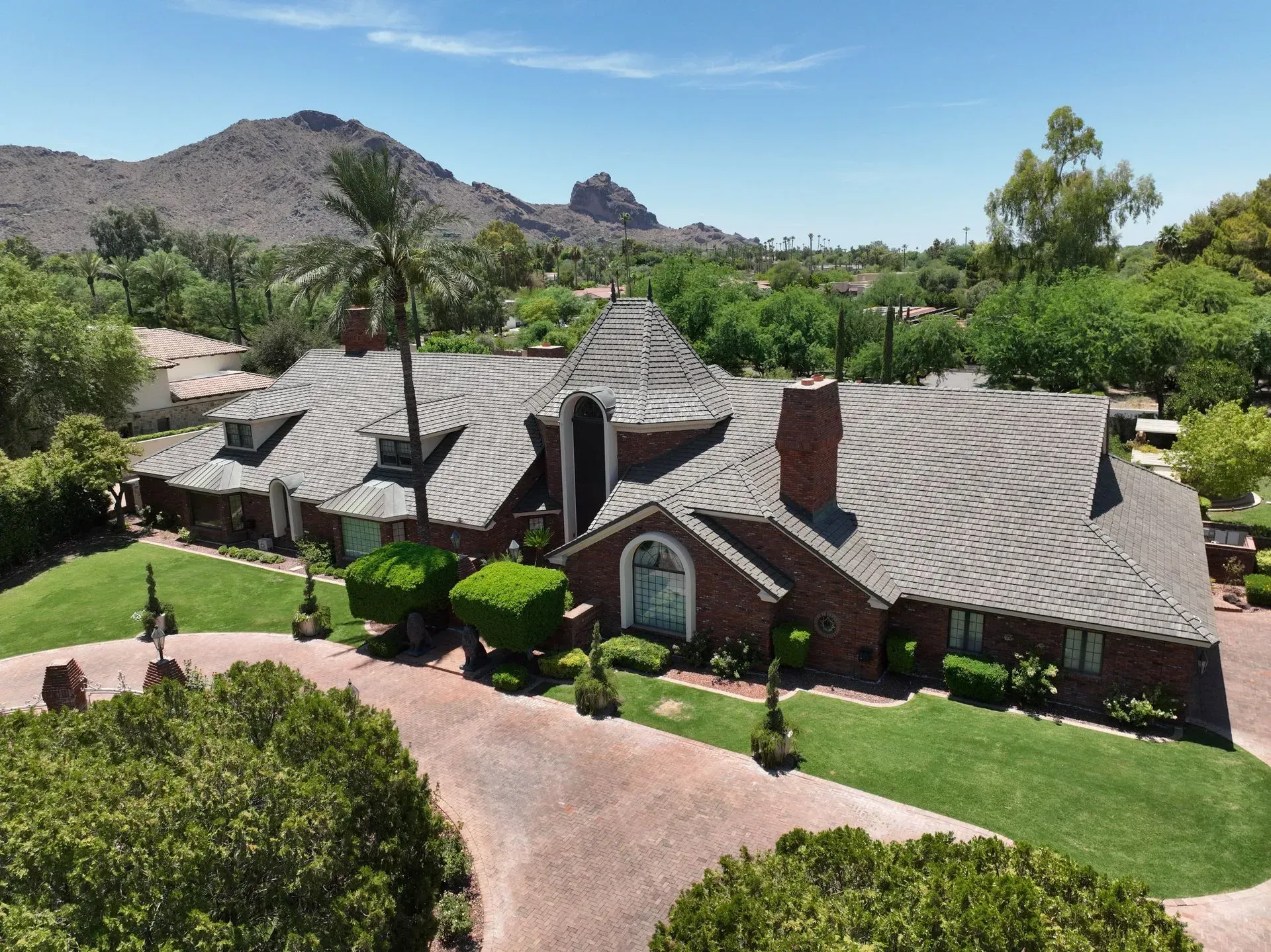 Aerial view of a large brick home with a curved roof, desert landscaping, and mountains in the background