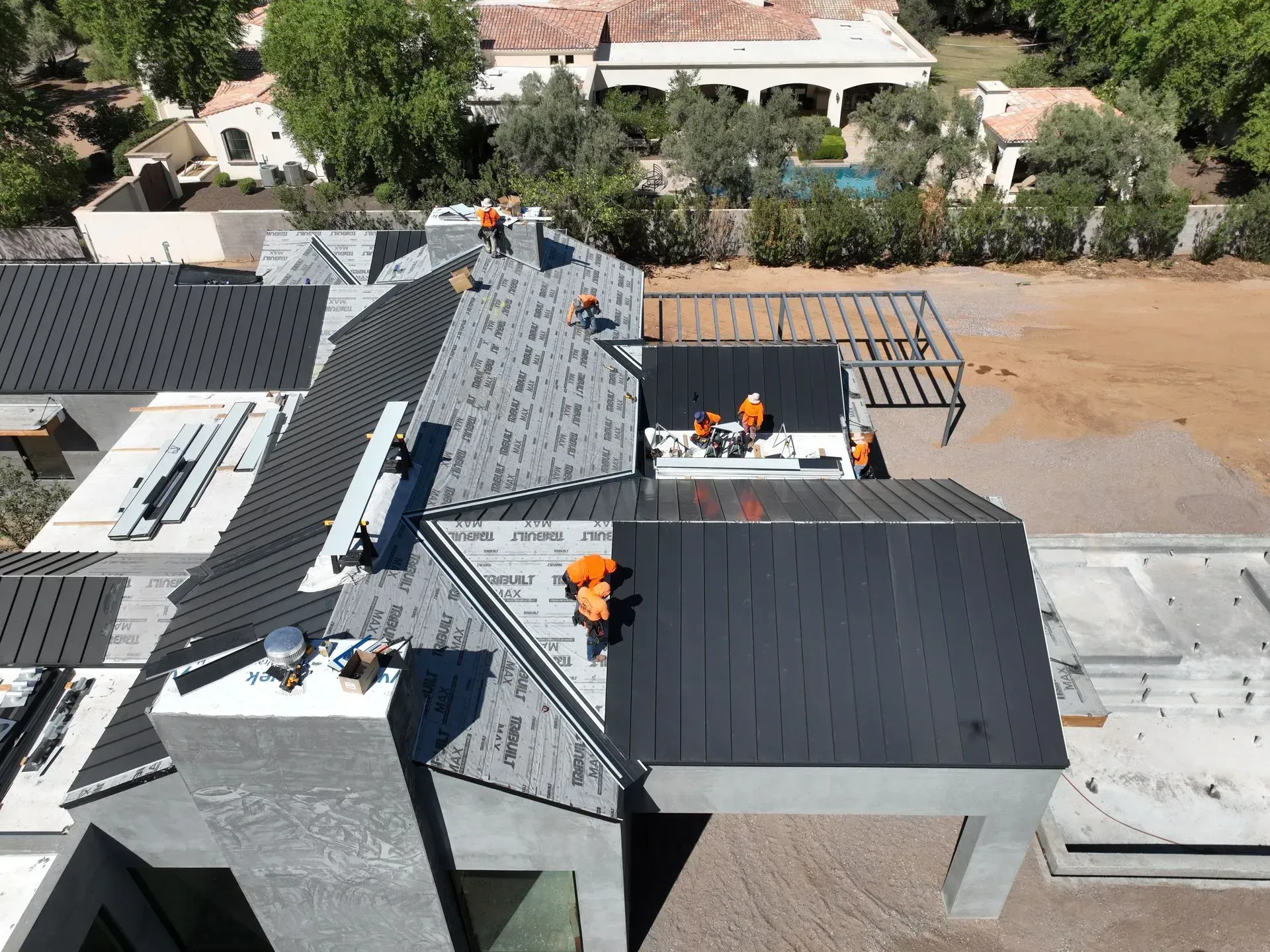 Roofers working on a gray shingled roof at a house construction site.