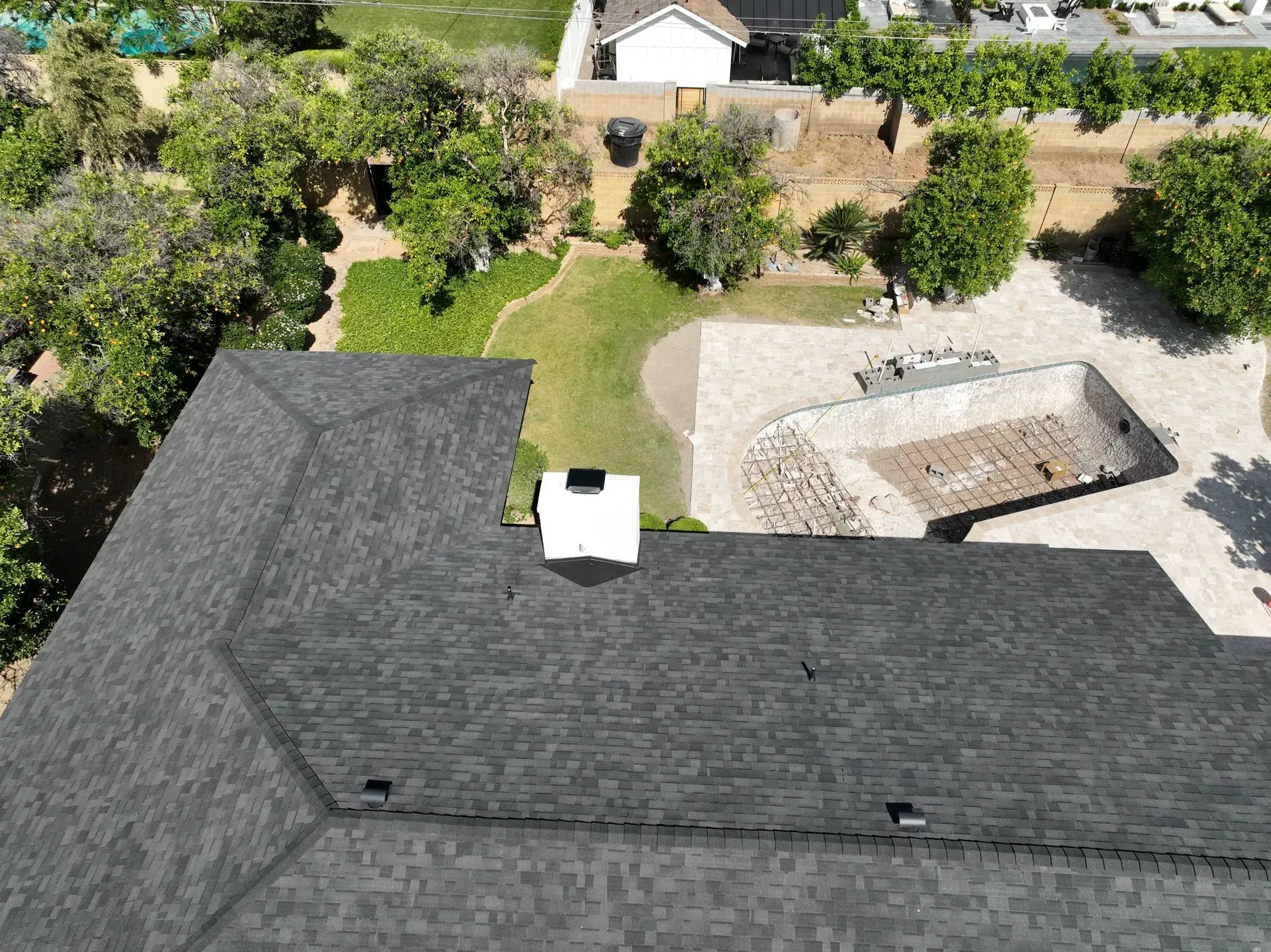 Aerial view of a house roof with chimney, trees, and a backyard patio with a fire pit.