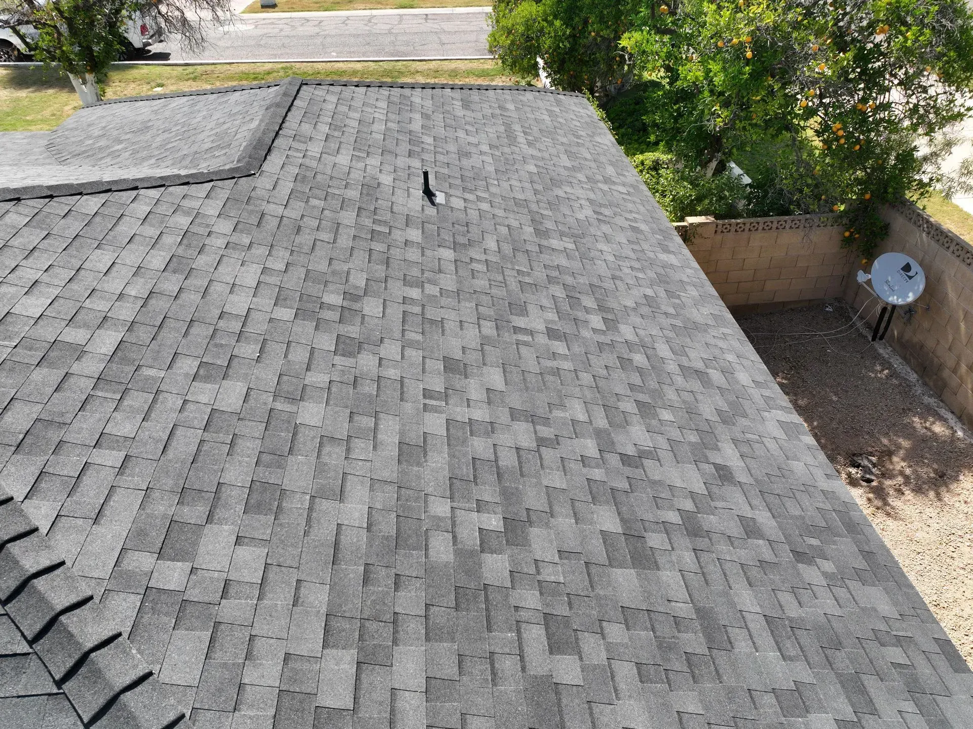Gray shingle roof with a small vent, trees and a satellite dish visible at the edge