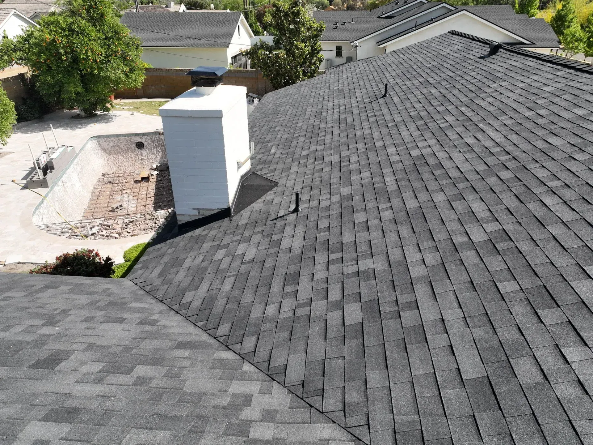 Rooftop view of gray shingles with a white chimney and neighboring houses in the background
