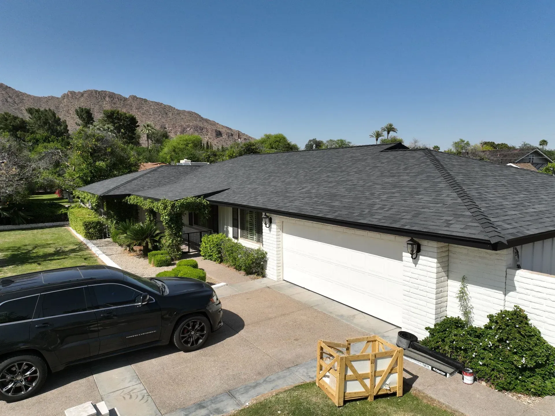 Single-story white house with dark roof, black car in driveway, and mountains in the background.
