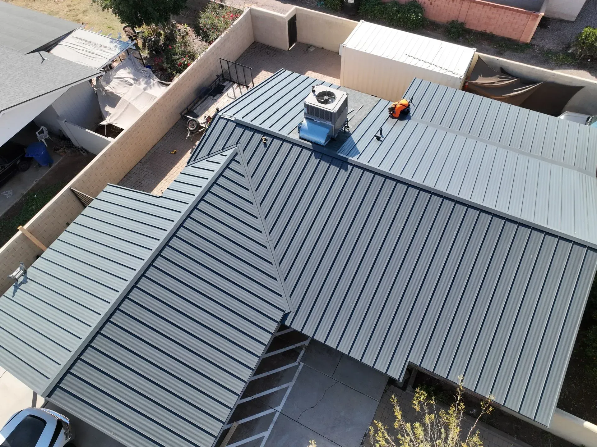 Aerial view of a gray metal roof with skylights, HVAC unit, and rooftop equipment in a residential area