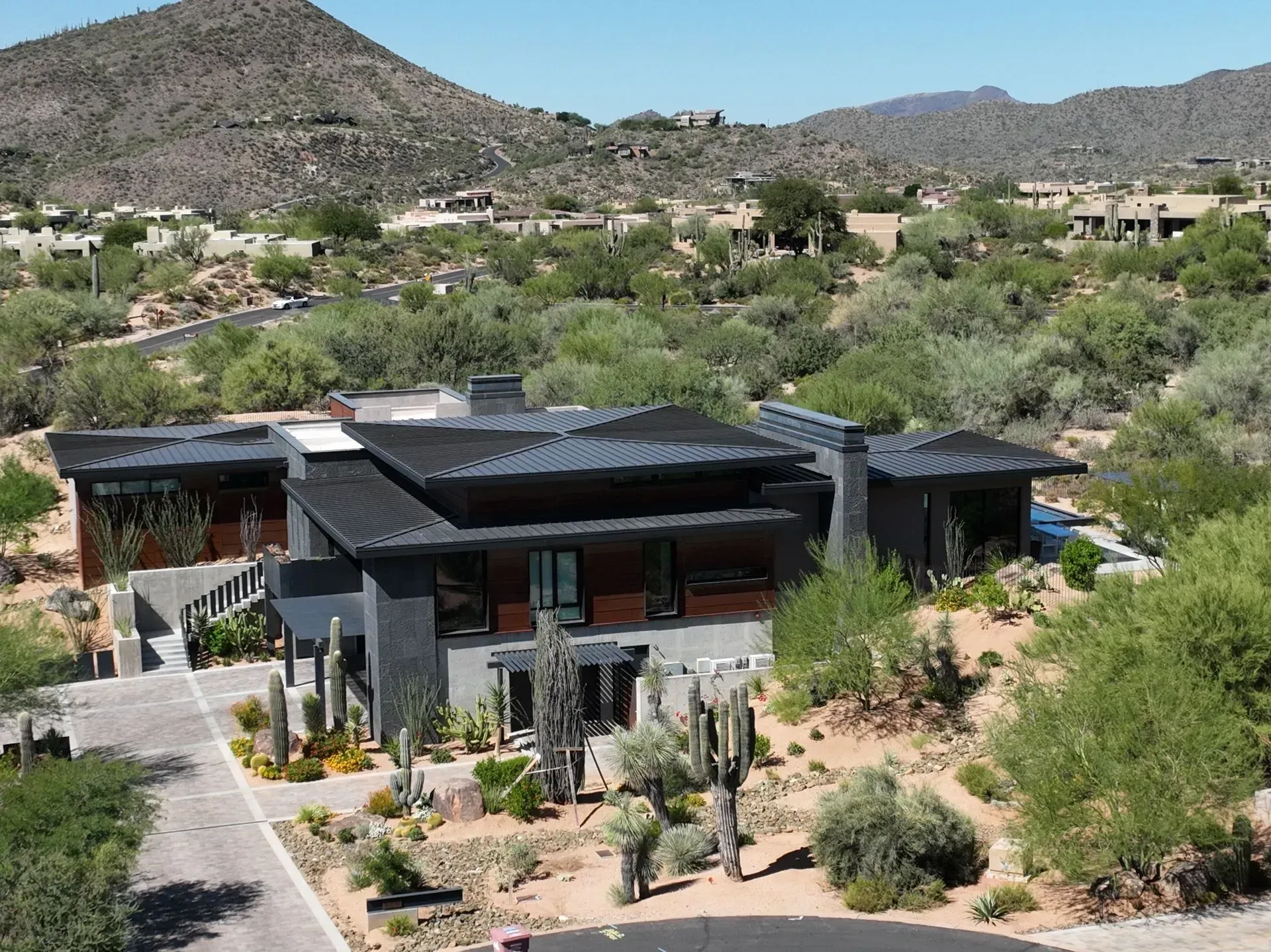 Modern dark-roofed house in a desert landscape with mountains and shrubs in the background