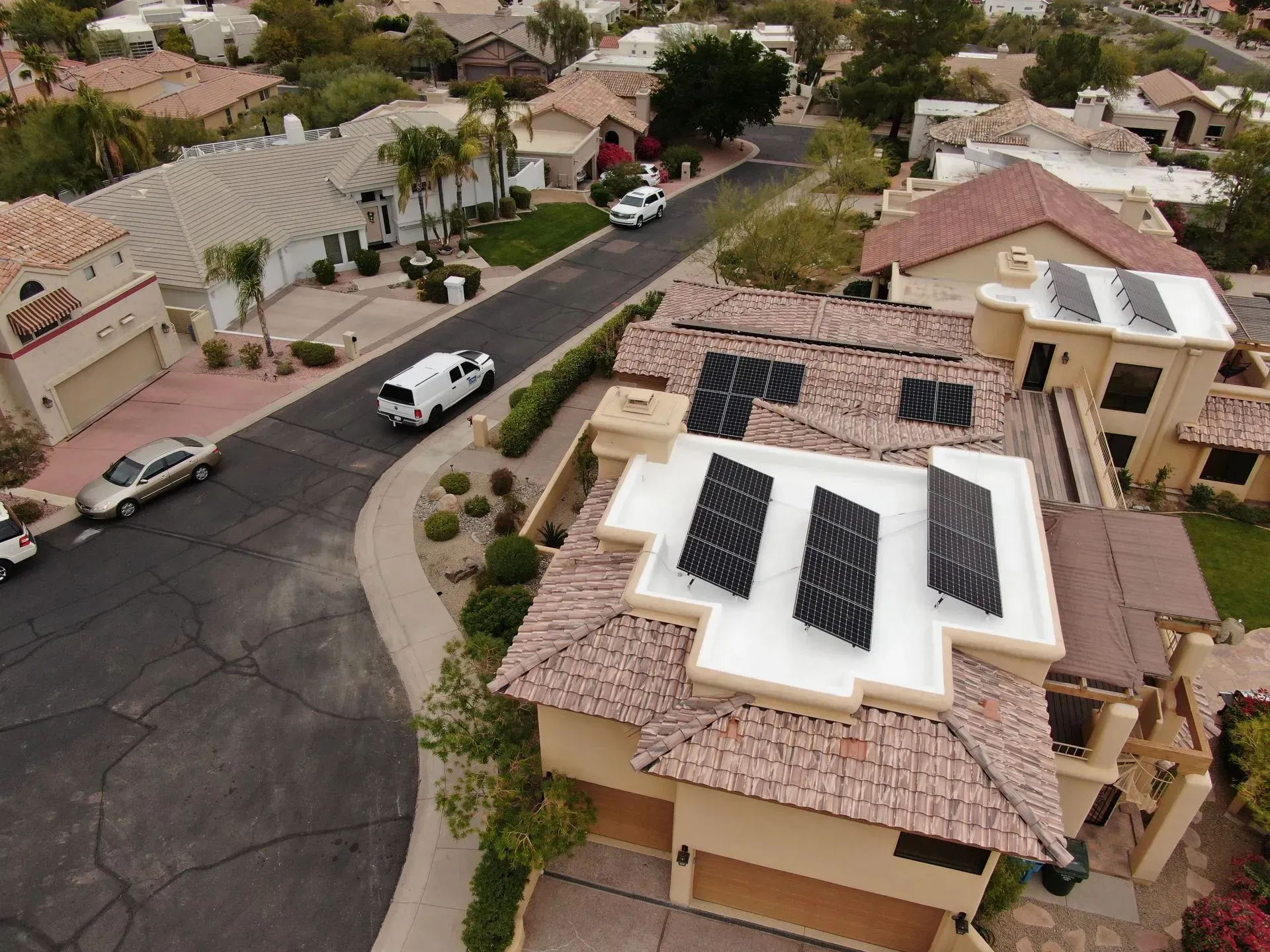 Aerial view of suburban homes on a curving street, with solar panels visible on several roofs.