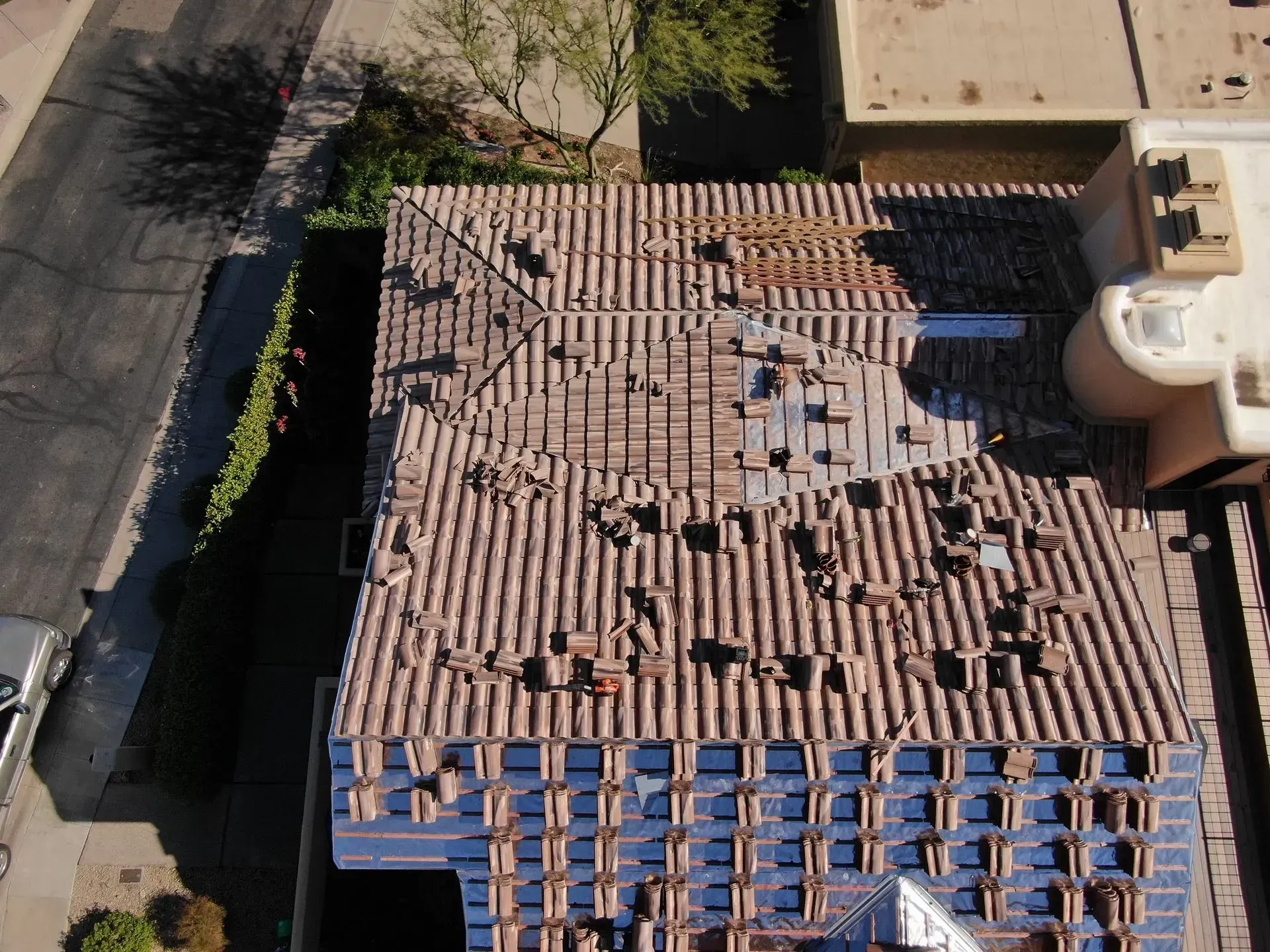 Aerial view of a roof with damaged tiles and debris beside a street and trees
