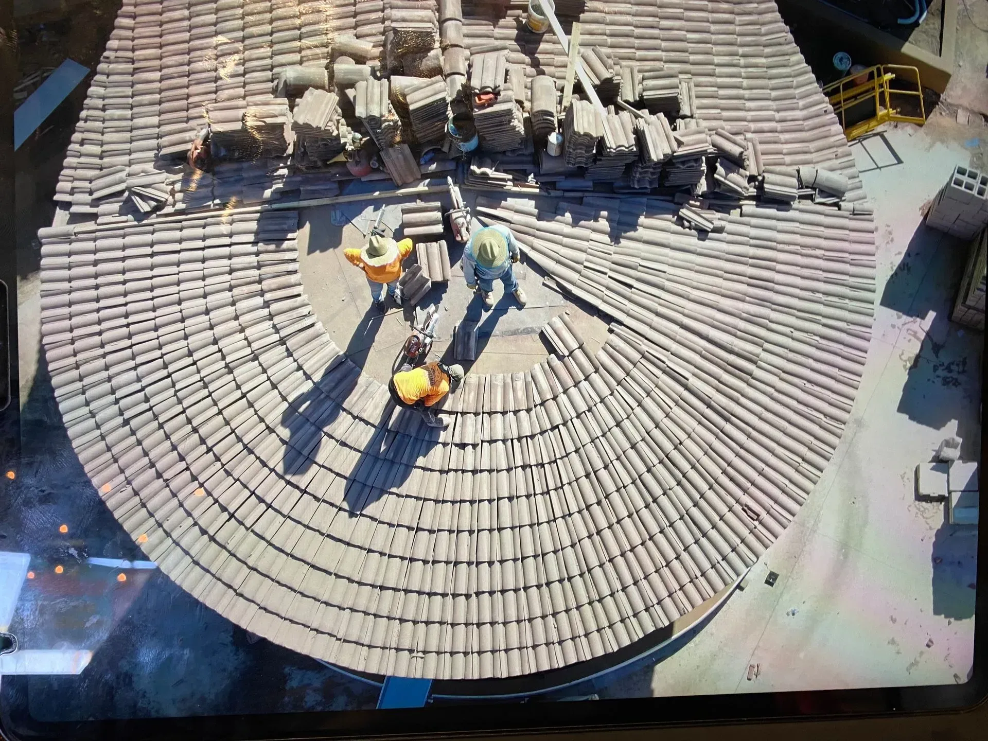 Workers on a circular tiled rooftop, repairing damaged shingles with tools and debris nearby