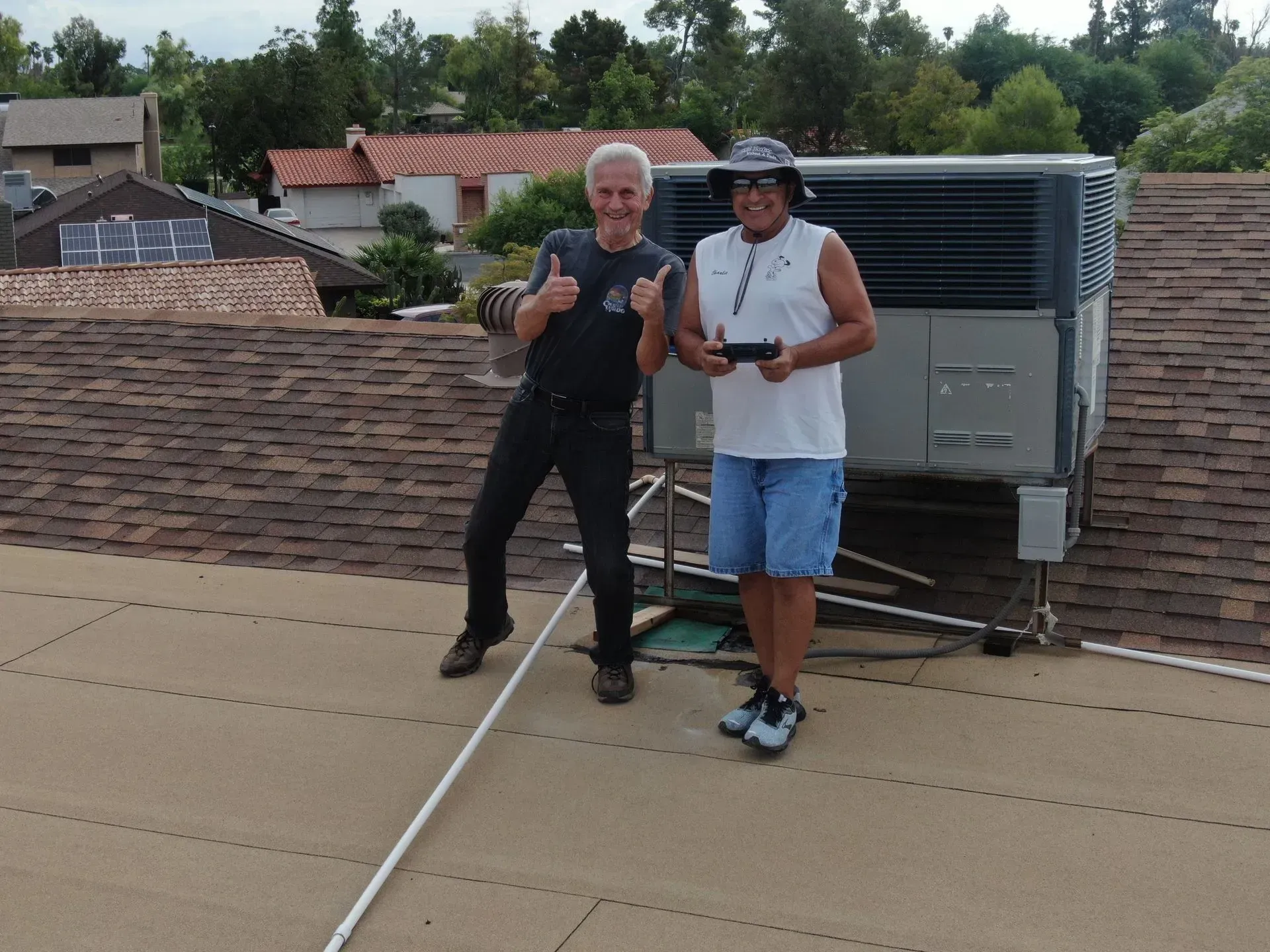 Two people standing on a rooftop beside HVAC equipment, smiling and giving thumbs-up.