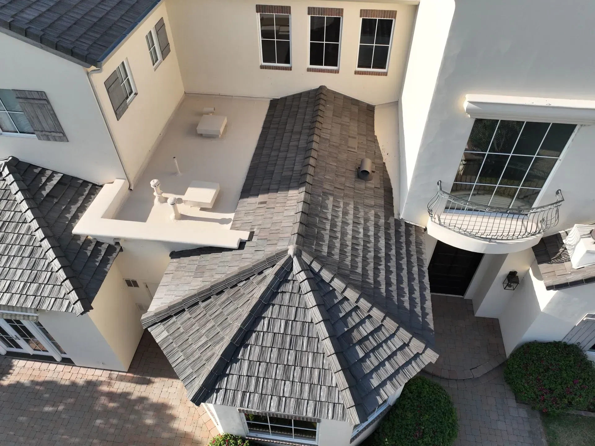 Aerial view of a house roof with gray shingles, white walls, and a small balcony courtyard.