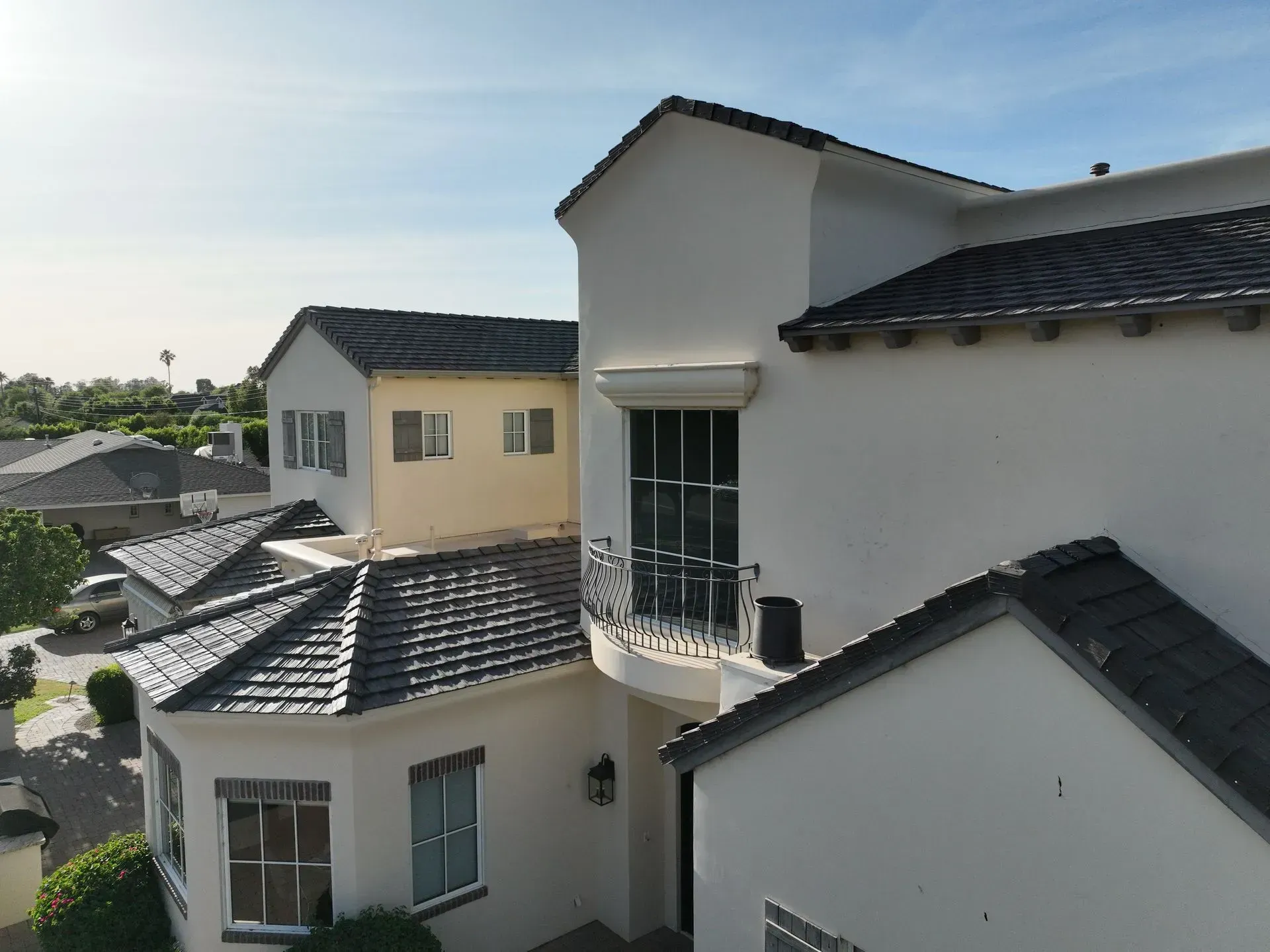White stucco houses with dark tile roofs on a sunny hillside, viewed from an elevated angle