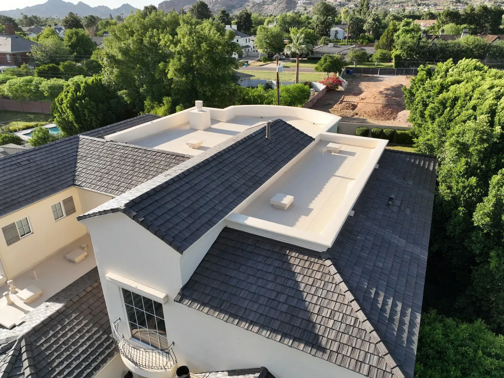 Aerial view of a house with a dark shingle roof surrounded by trees in a suburban neighborhood