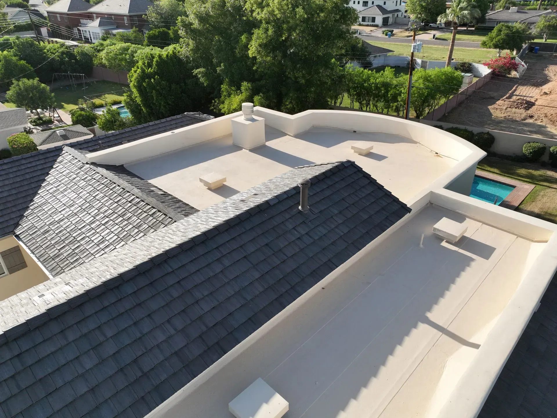 Aerial view of a modern house roof with white and dark gray sections in a suburban neighborhood