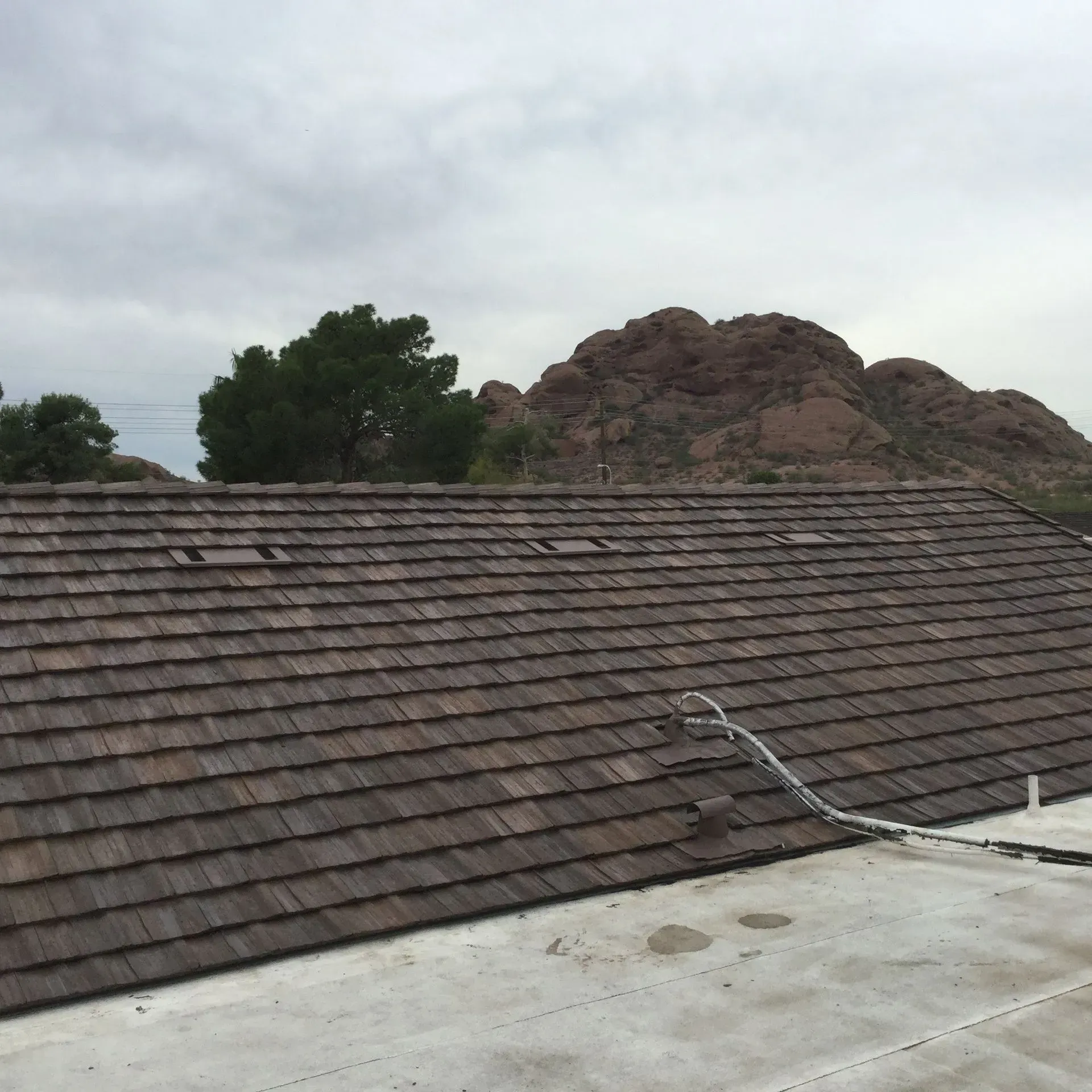 Tile roof with a white rooftop and rocky hill in the background under a cloudy sky