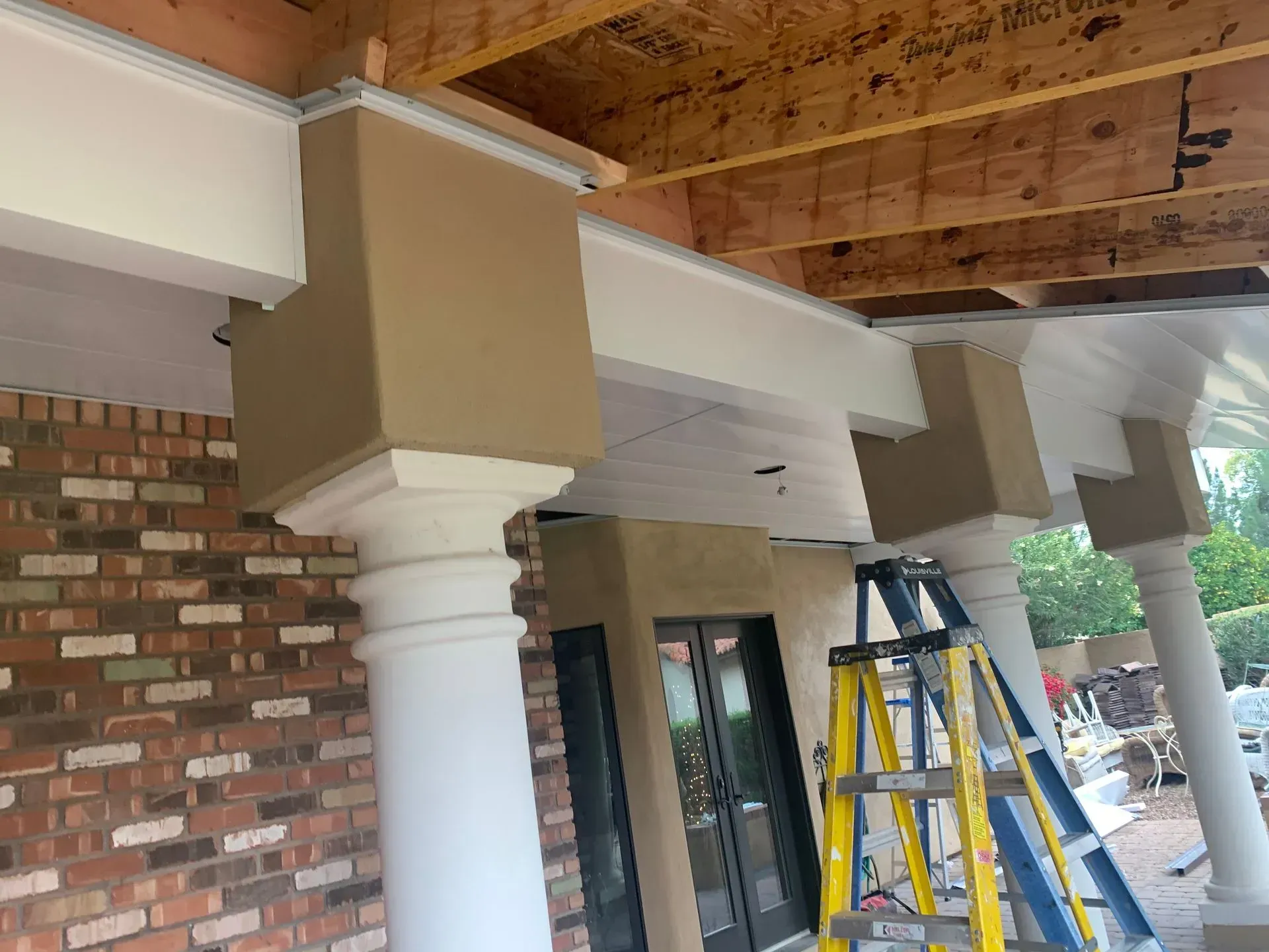 Covered storefront porch with brick columns, tan beams, and a ladder on the sidewalk