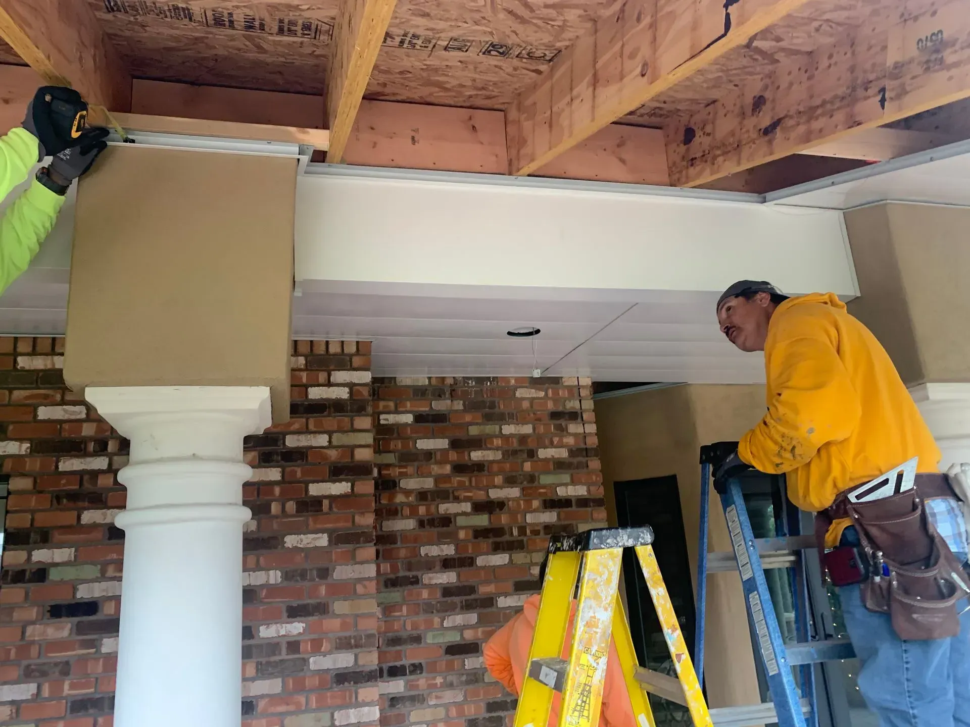 Worker installing trim above a brick fireplace in a room with exposed ceiling beams